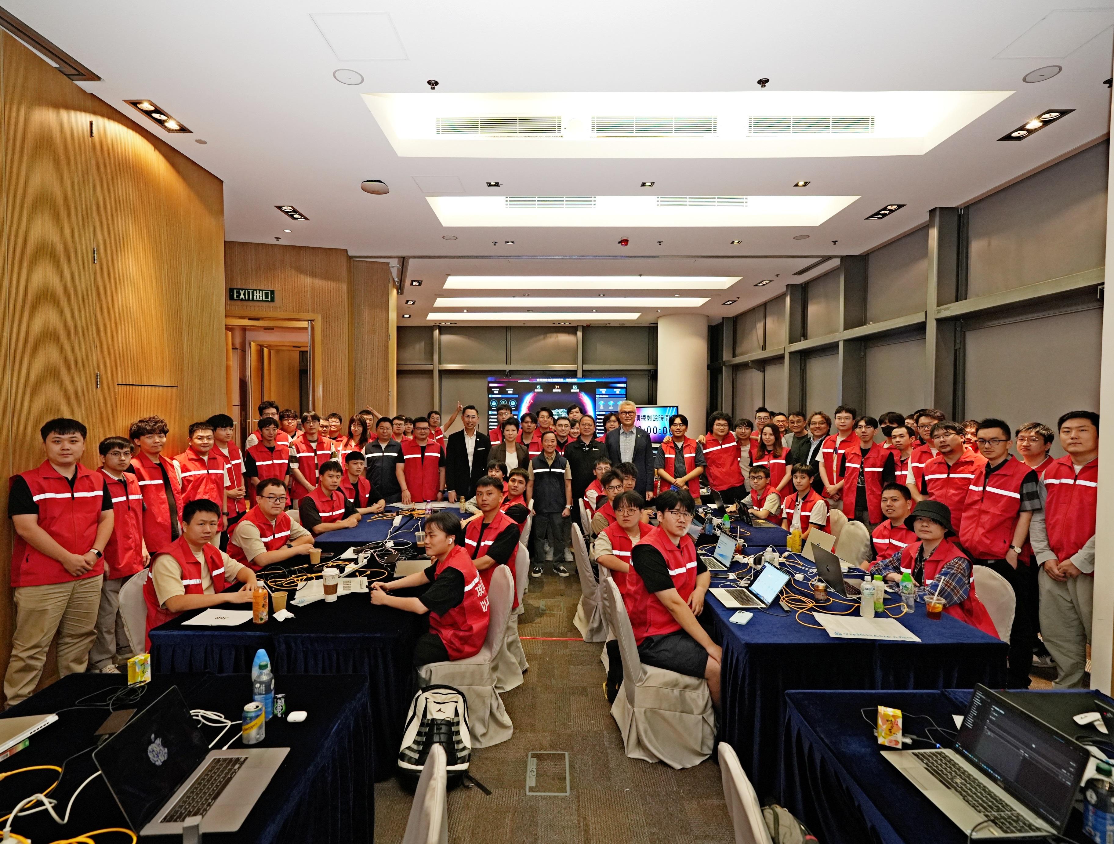 「香港網絡安全攻防演練—以攻築防2025」昨晚（十月十二日）圓滿結束。圖示數字政策專員黃志光（站立，第一排中）在演練場地與協辦單位代表、參賽隊伍和工作人員合照。